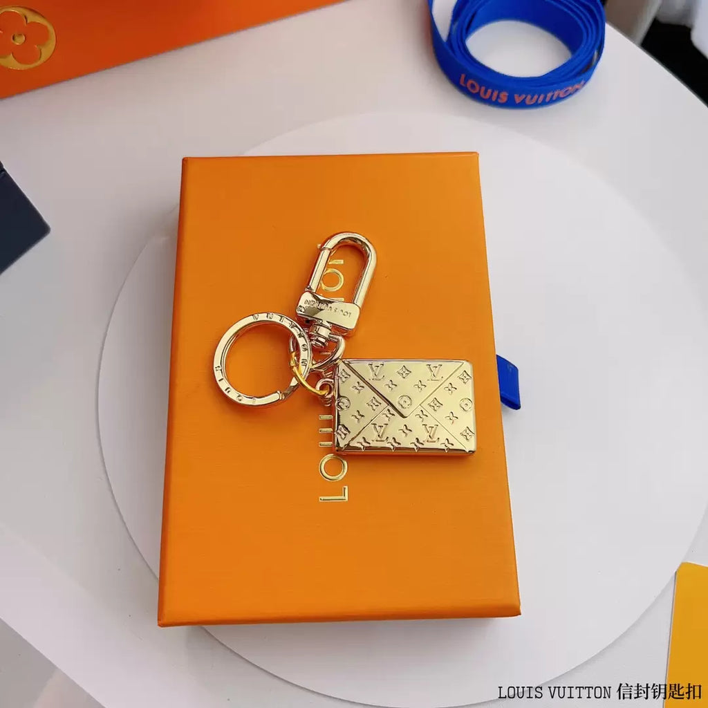 Gold-tone envelope charm and round keyring on an orange box