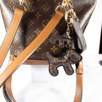 Monogram dog keychain and wrist strap attached to a brown bag
