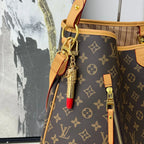 Gold-tone lipstick charm attached to a brown monogram bag