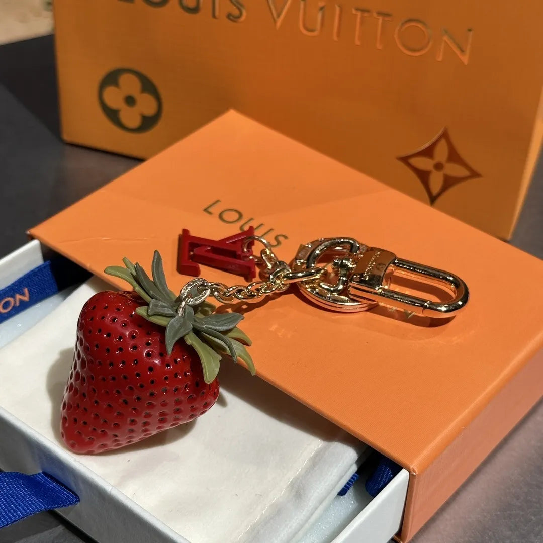 Red strawberry keychain with green leaves beside orange packaging