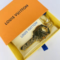 Gold-tone key-shaped LV charm resting inside an orange box